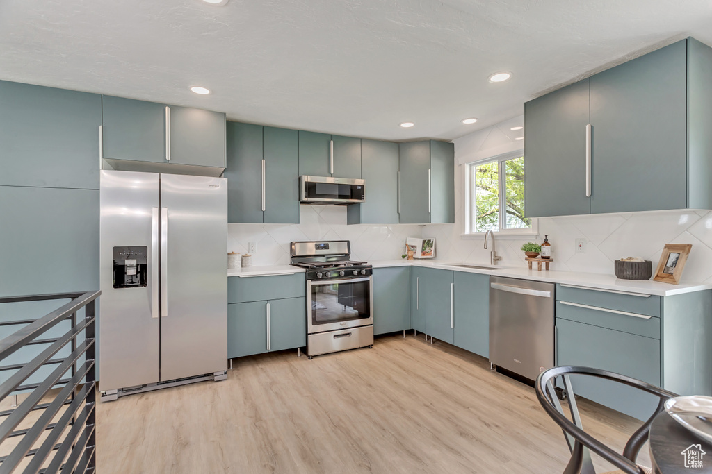 Kitchen with backsplash, light hardwood / wood-style flooring, sink, and stainless steel appliances