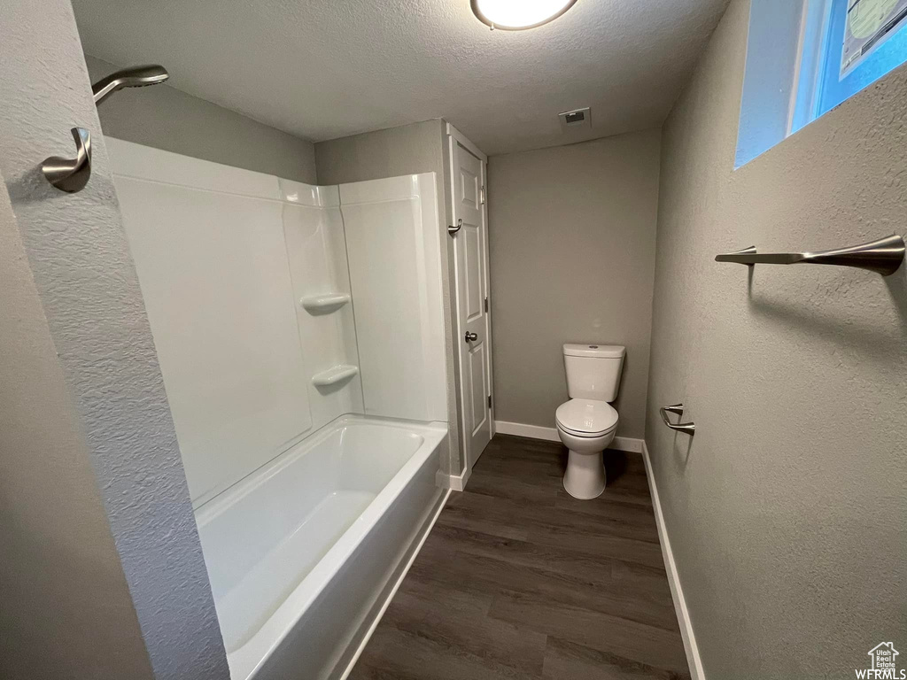 Bathroom with wood-type flooring, a textured ceiling, bathtub / shower combination, and toilet