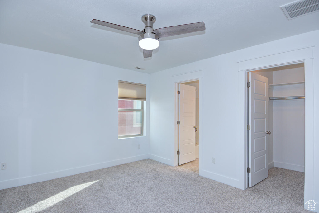 Unfurnished bedroom with light colored carpet, a spacious closet, ceiling fan, and a closet