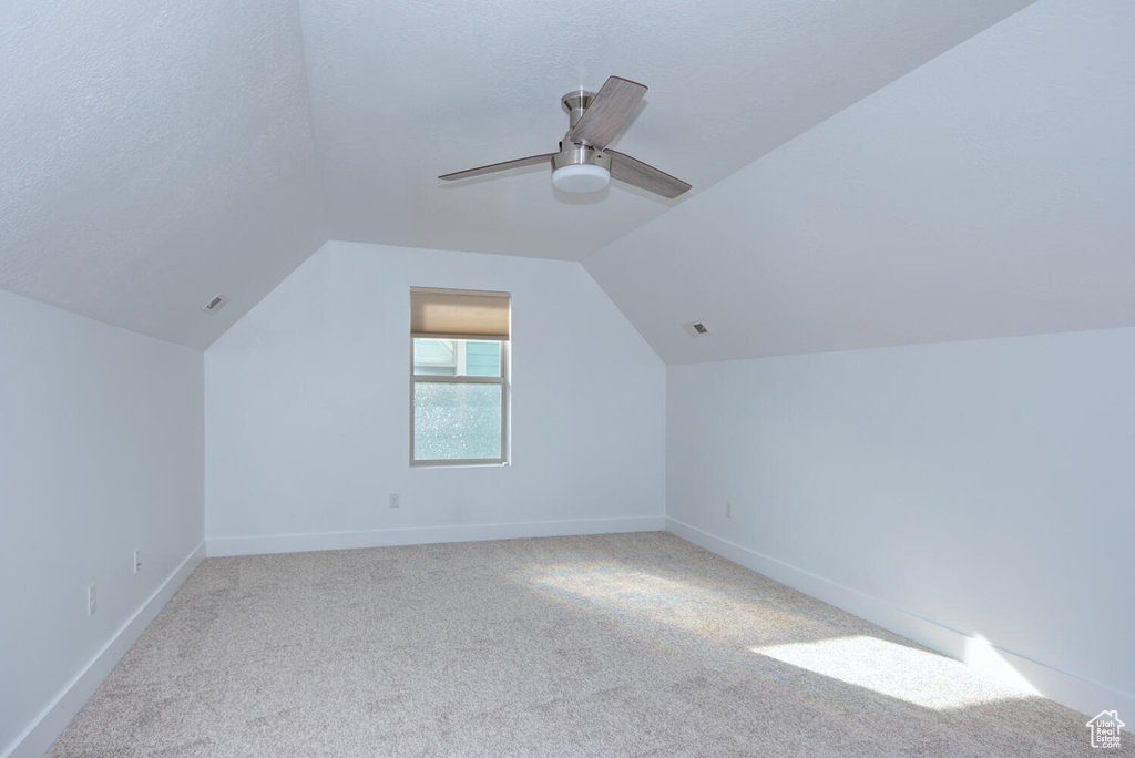 Additional living space with light colored carpet, lofted ceiling, ceiling fan, and a textured ceiling
