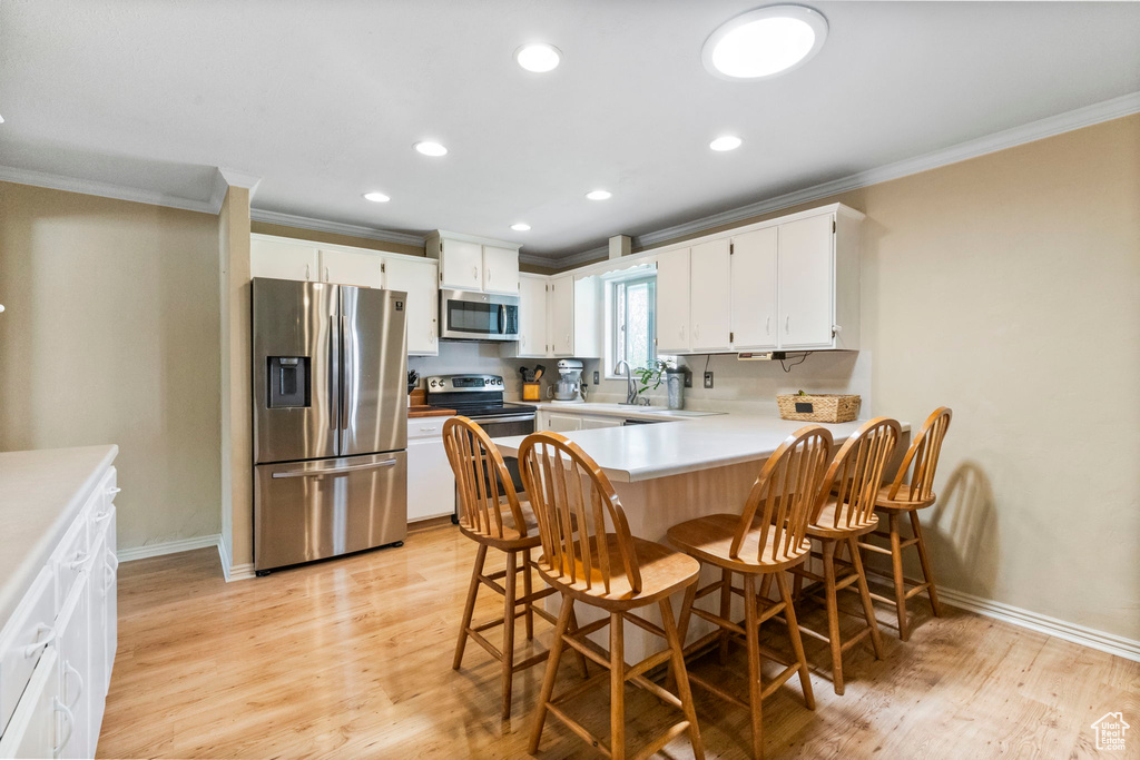 Kitchen with white cabinets, crown molding, appliances with stainless steel finishes, a kitchen bar, and light hardwood / wood-style floors