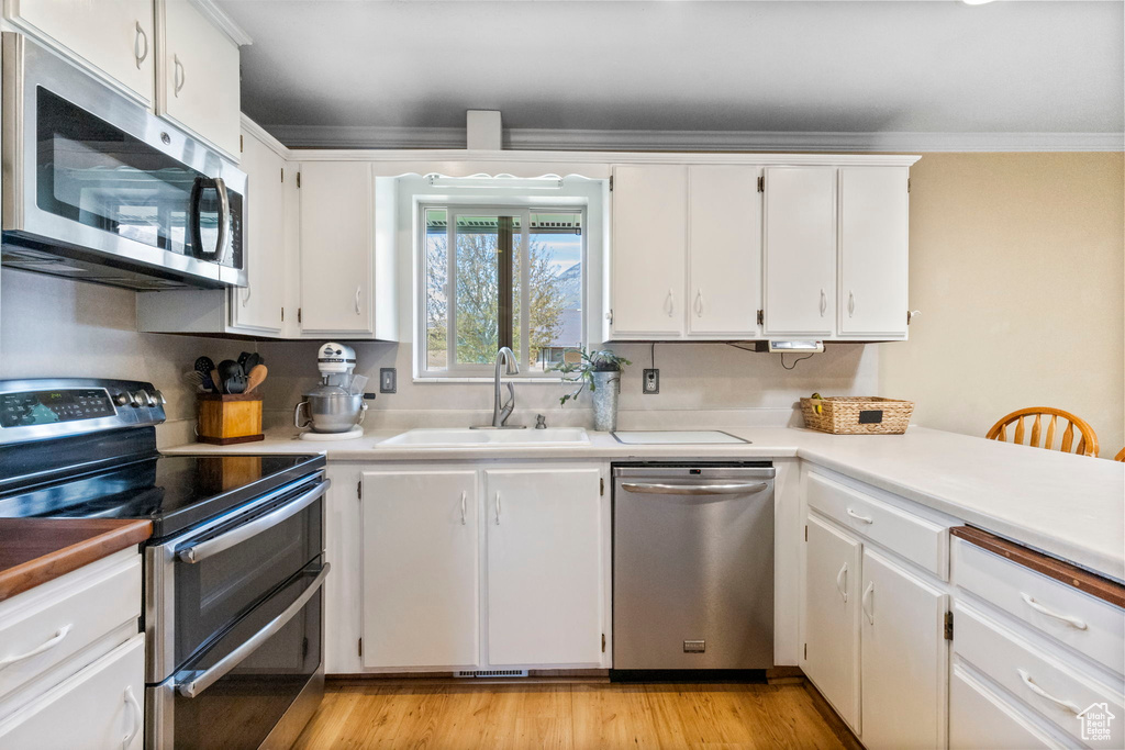 Kitchen with appliances with stainless steel finishes, light hardwood / wood-style floors, white cabinets, and sink