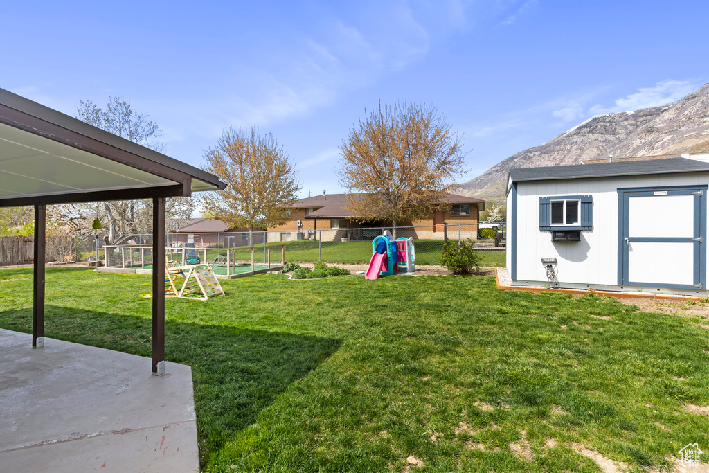 View of yard featuring a patio area, a mountain view, a playground, and a storage shed