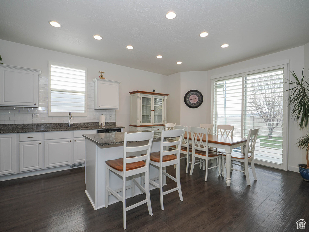 Kitchen with tasteful backsplash, white cabinetry, a kitchen island, and dark wood-type flooring