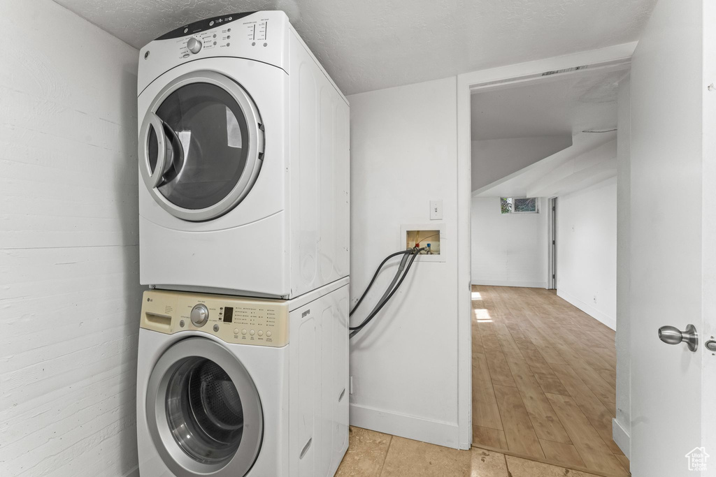 Clothes washing area featuring hookup for a washing machine, light hardwood / wood-style flooring, a textured ceiling, and stacked washer / drying machine