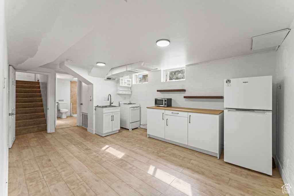 Kitchen featuring white appliances, washer / dryer, white cabinetry, sink, and light wood-type flooring