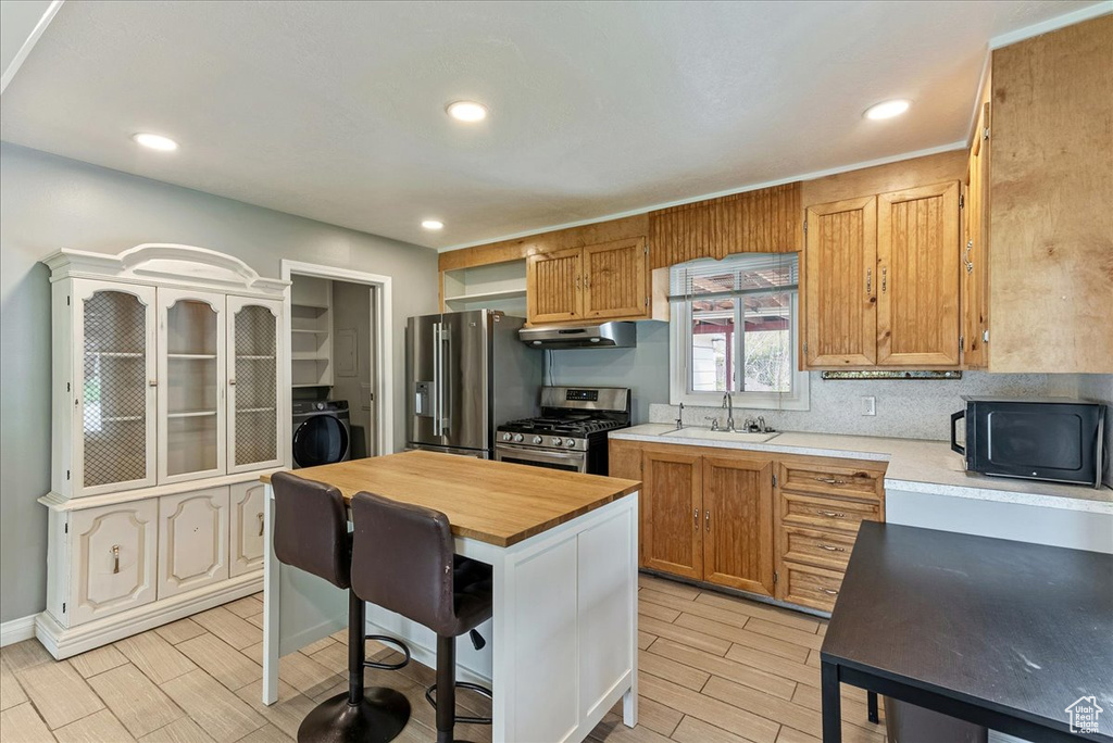 Kitchen featuring appliances with stainless steel finishes, a kitchen island, a breakfast bar area, washer / clothes dryer, and sink