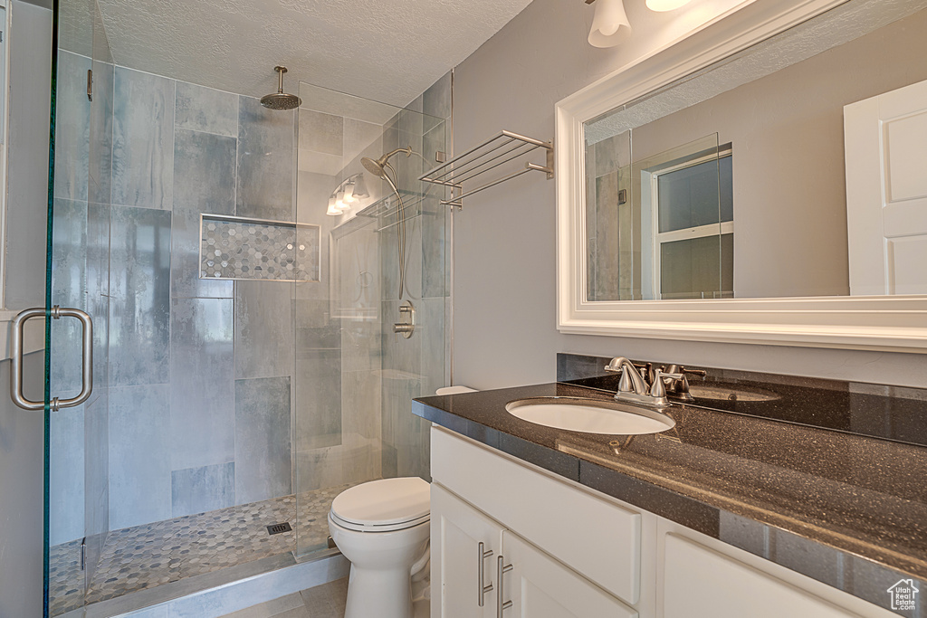 Bathroom with a shower with shower door, toilet, oversized vanity, and a textured ceiling