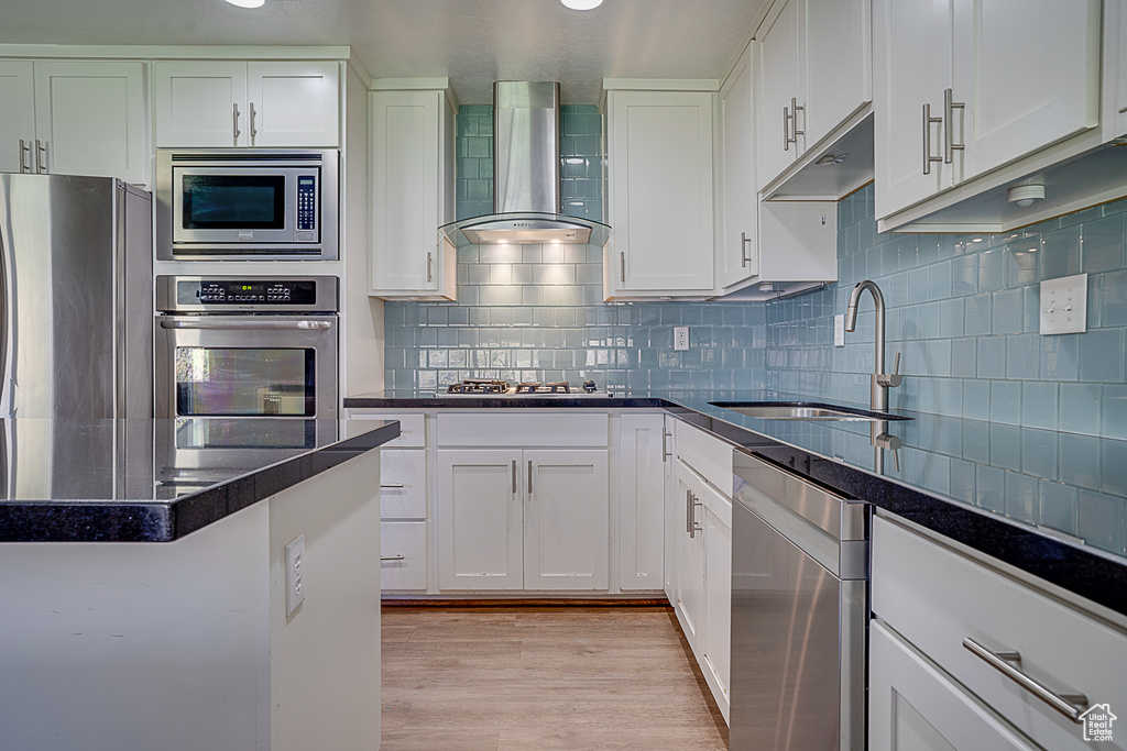 Kitchen featuring sink, wall chimney range hood, backsplash, stainless steel appliances, and light hardwood / wood-style flooring