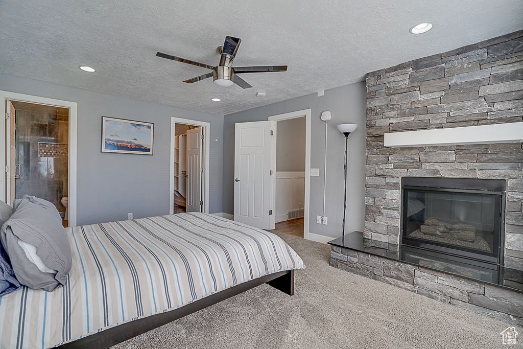 Carpeted bedroom featuring a stone fireplace, ensuite bath, ceiling fan, and a textured ceiling