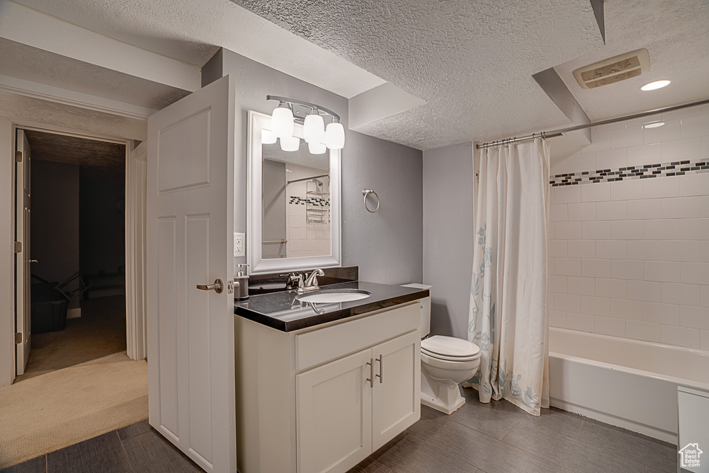 Full bathroom with vanity with extensive cabinet space, a textured ceiling, shower / tub combo, tile floors, and toilet