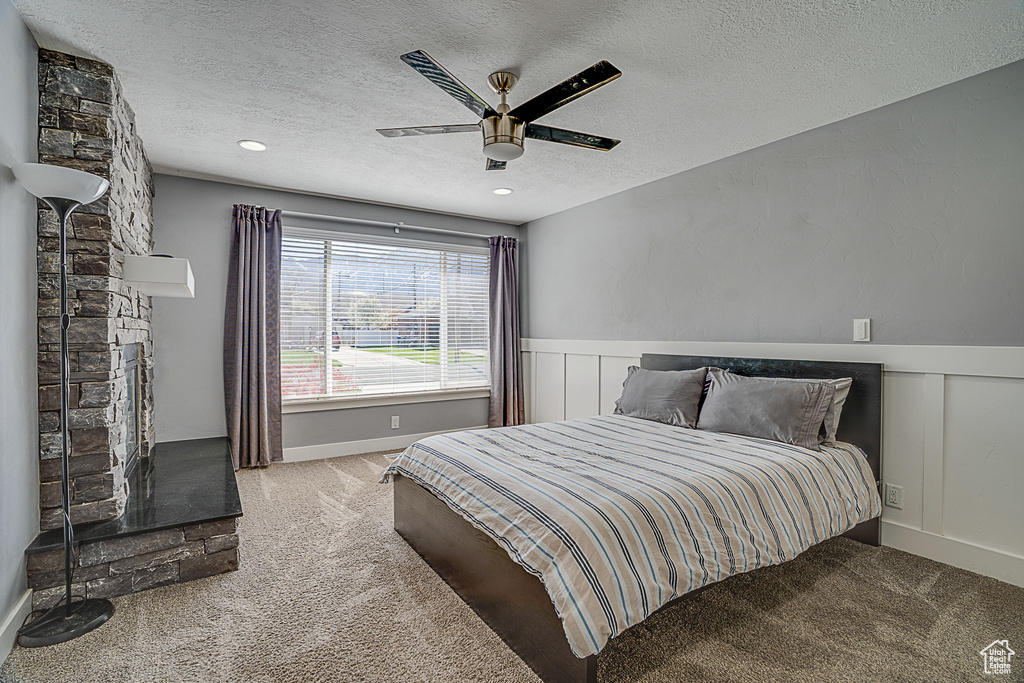 Carpeted bedroom with ceiling fan, a fireplace, and a textured ceiling