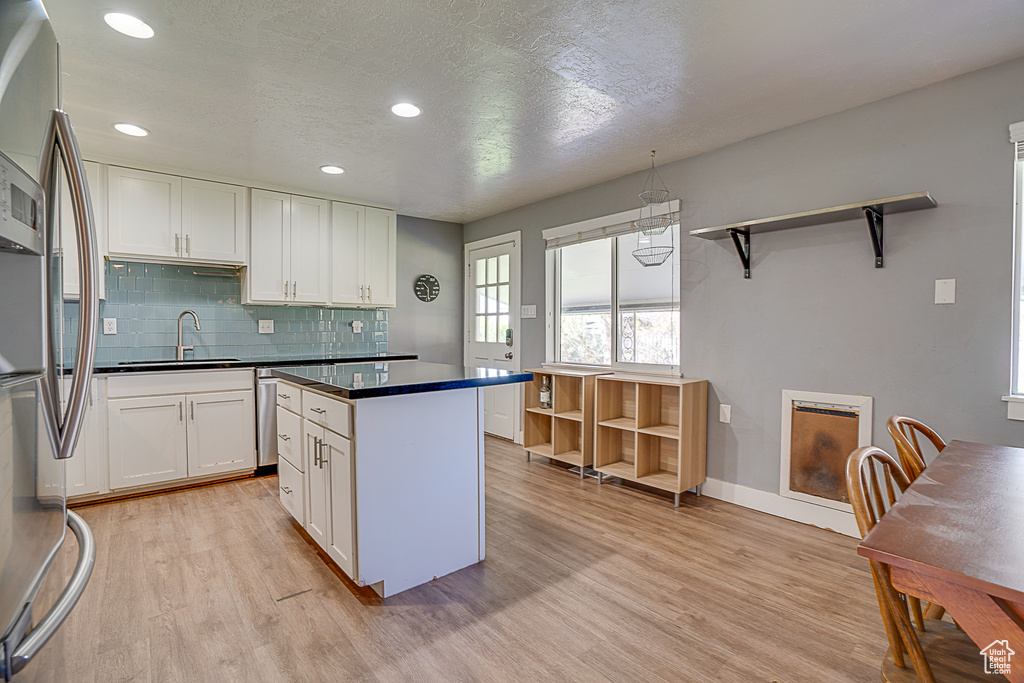 Kitchen featuring backsplash, a kitchen island, white cabinets, sink, and light wood-type flooring
