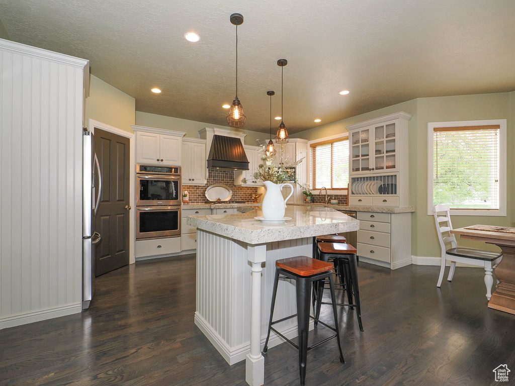 Kitchen featuring a kitchen island, custom range hood, tasteful backsplash, dark wood-type flooring, and white cabinetry