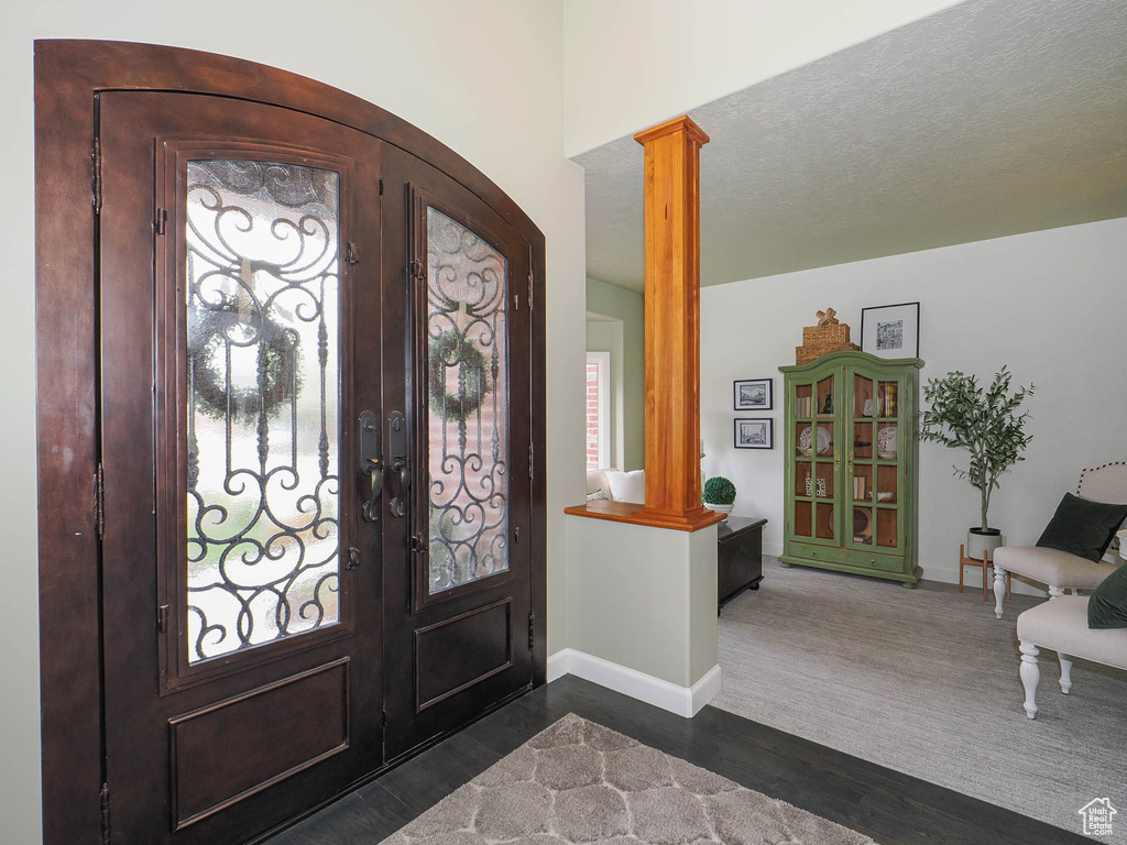 Entryway with a textured ceiling, ornate columns, dark colored carpet, and french doors