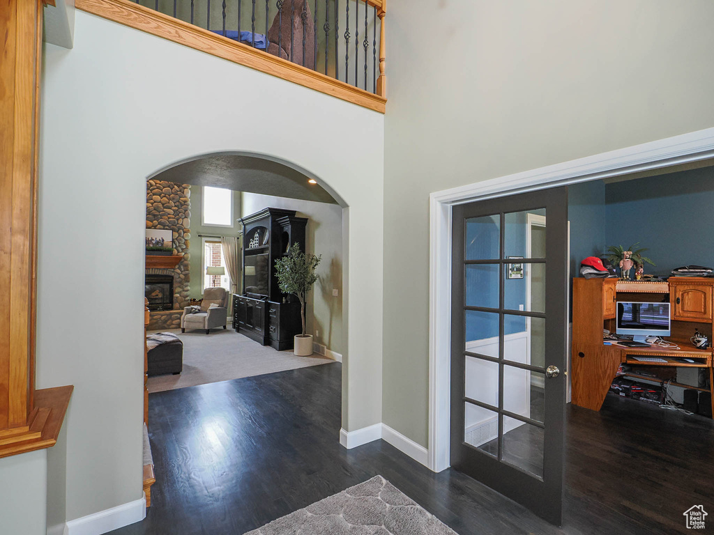 Entrance foyer with french doors, a stone fireplace, dark wood-type flooring, and a towering ceiling