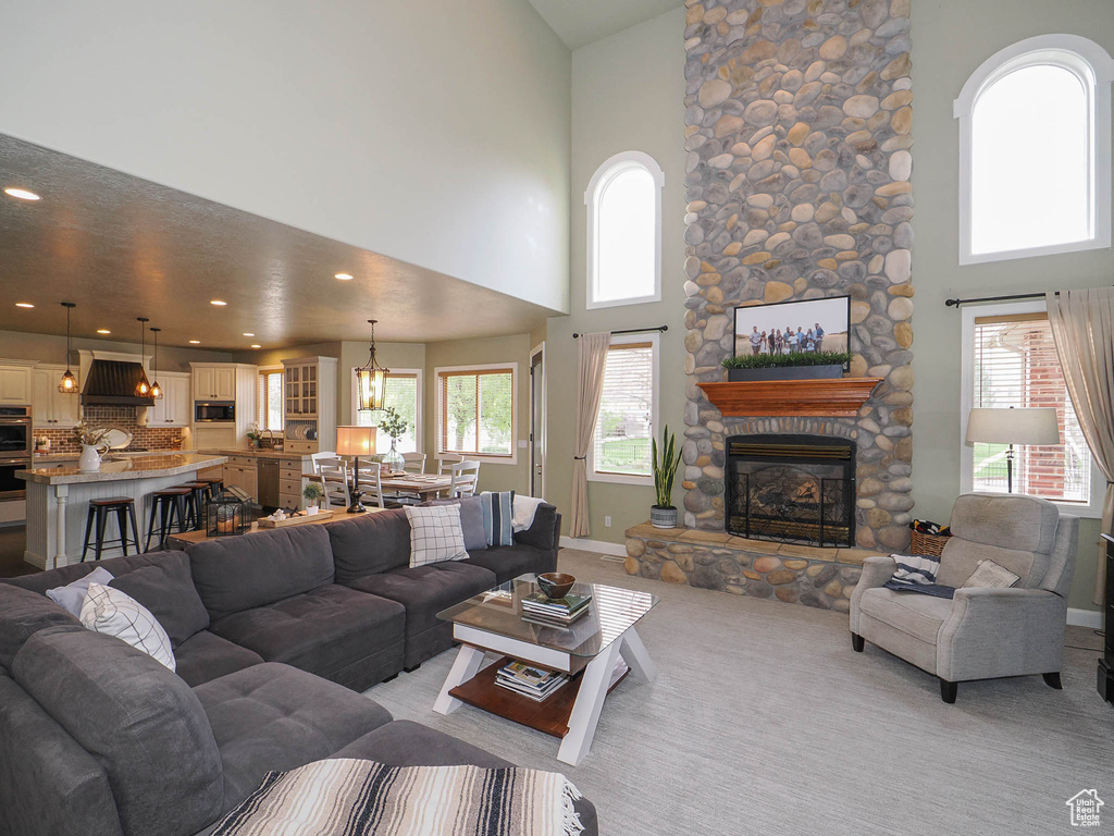Living room with light colored carpet, a high ceiling, a stone fireplace, and a wealth of natural light