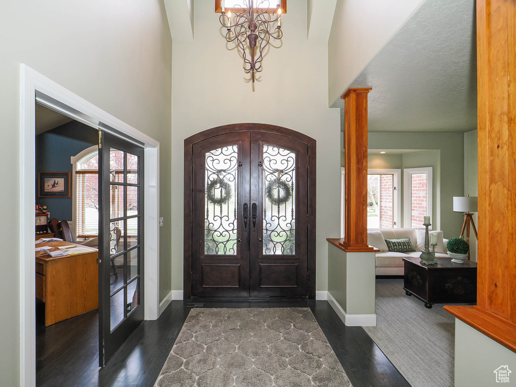 Foyer with french doors, ornate columns, dark hardwood / wood-style floors, and a chandelier