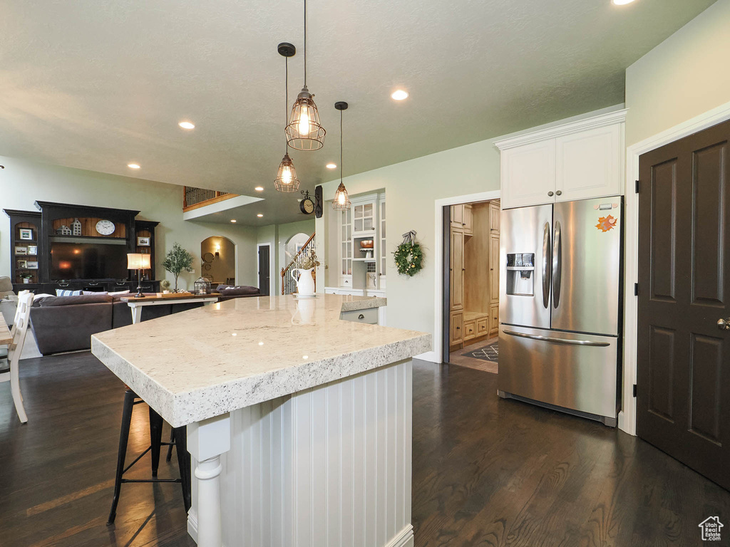 Kitchen featuring stainless steel fridge with ice dispenser, a kitchen bar, an island with sink, white cabinets, and dark hardwood / wood-style flooring