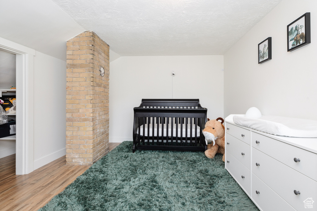 Bedroom featuring light wood-type flooring, brick wall, ornate columns, a crib, and a textured ceiling