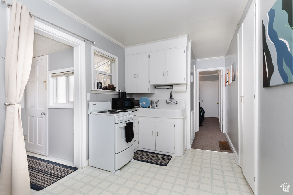 Kitchen featuring white range, crown molding, light tile flooring, and white cabinetry