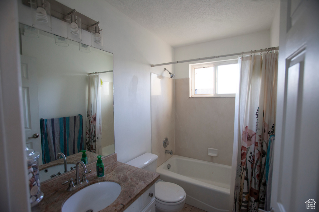 Full bathroom featuring a textured ceiling, toilet, vanity, and shower / tub combo with curtain