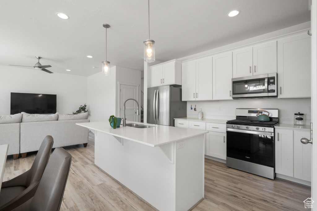 Kitchen featuring appliances with stainless steel finishes, a kitchen bar, sink, light hardwood / wood-style flooring, and a kitchen island with sink