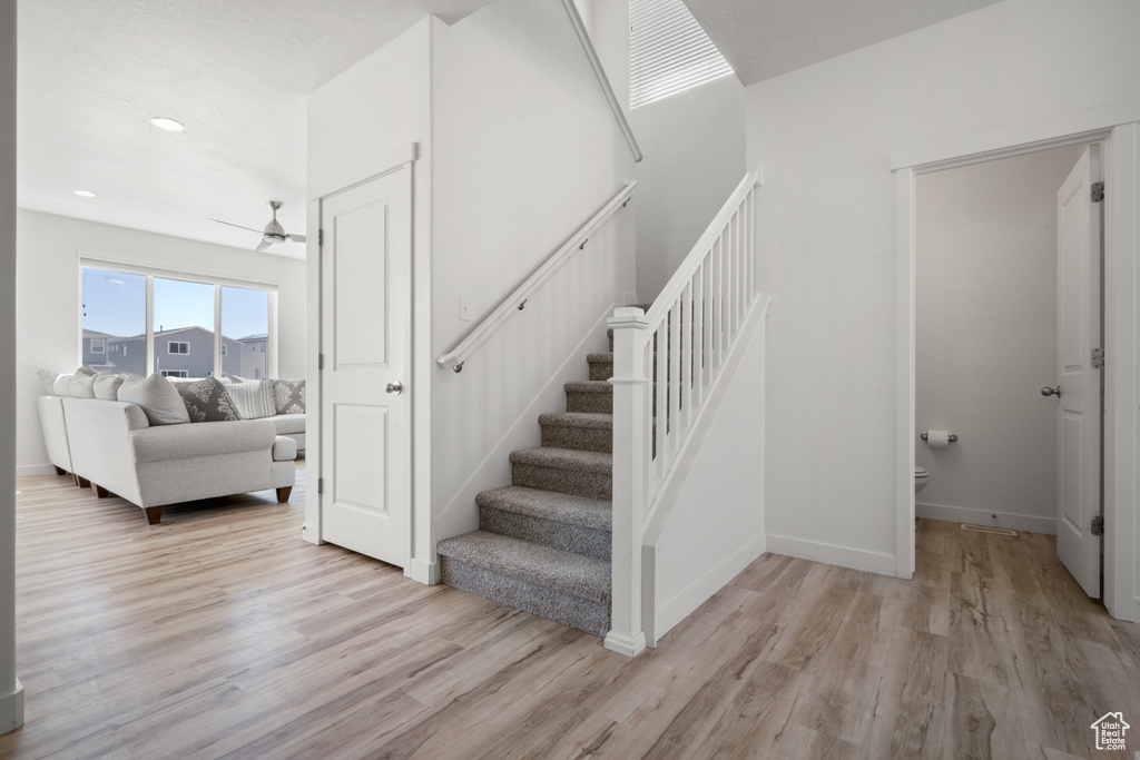Stairway with light hardwood / wood-style flooring and ceiling fan