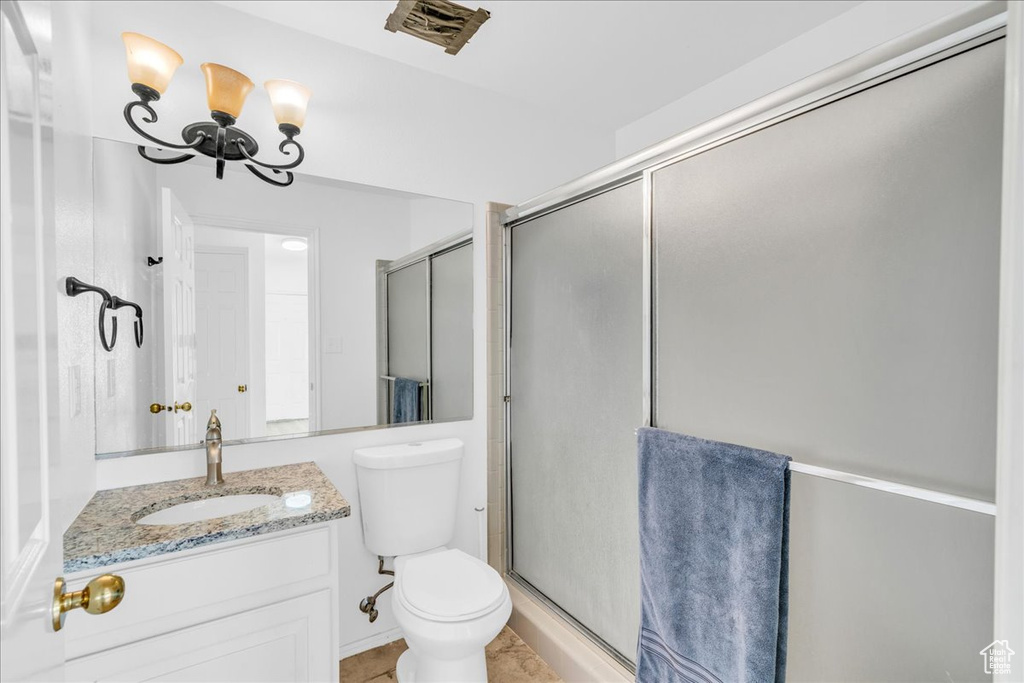 Bathroom featuring tile flooring, toilet, a shower with shower door, vanity, and an inviting chandelier