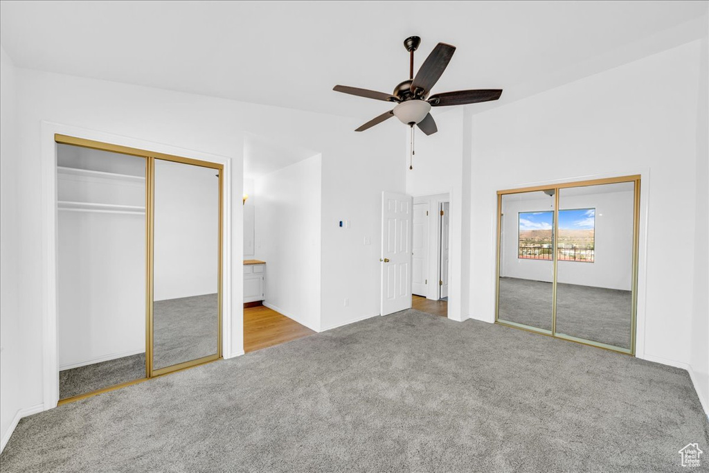 Unfurnished bedroom featuring lofted ceiling, light carpet, ceiling fan, and multiple closets
