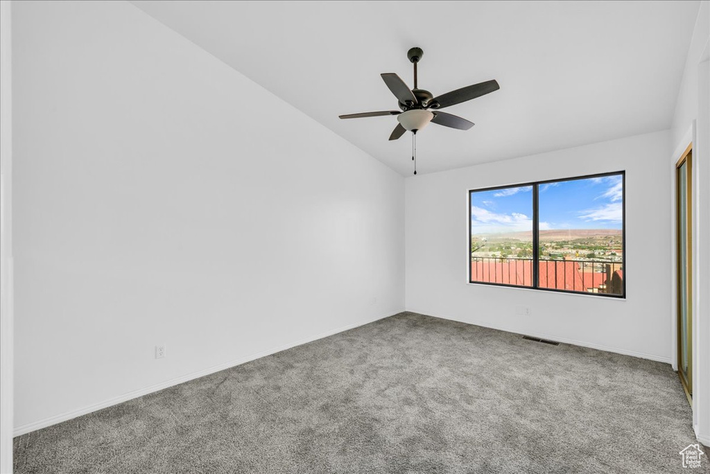 Empty room featuring light colored carpet, ceiling fan, and vaulted ceiling