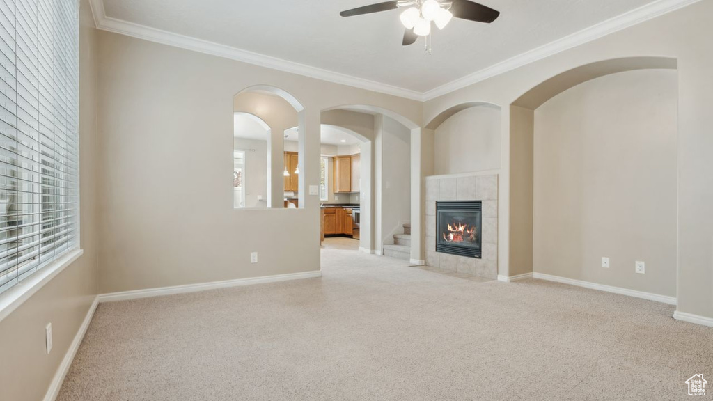 Unfurnished living room with light colored carpet, ceiling fan, crown molding, and a tiled fireplace