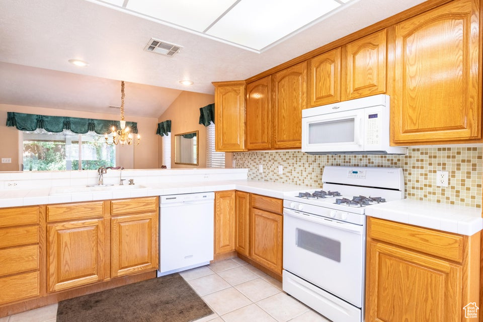 Kitchen with tasteful backsplash, white appliances, light tile floors, and lofted ceiling