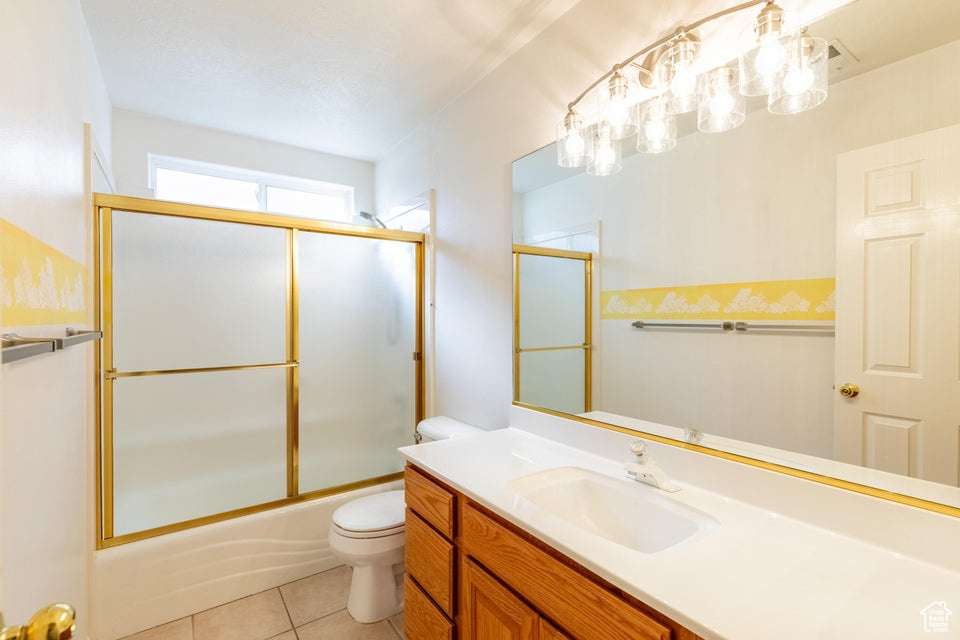 Full bathroom with enclosed tub / shower combo, tile floors, vanity, and toilet