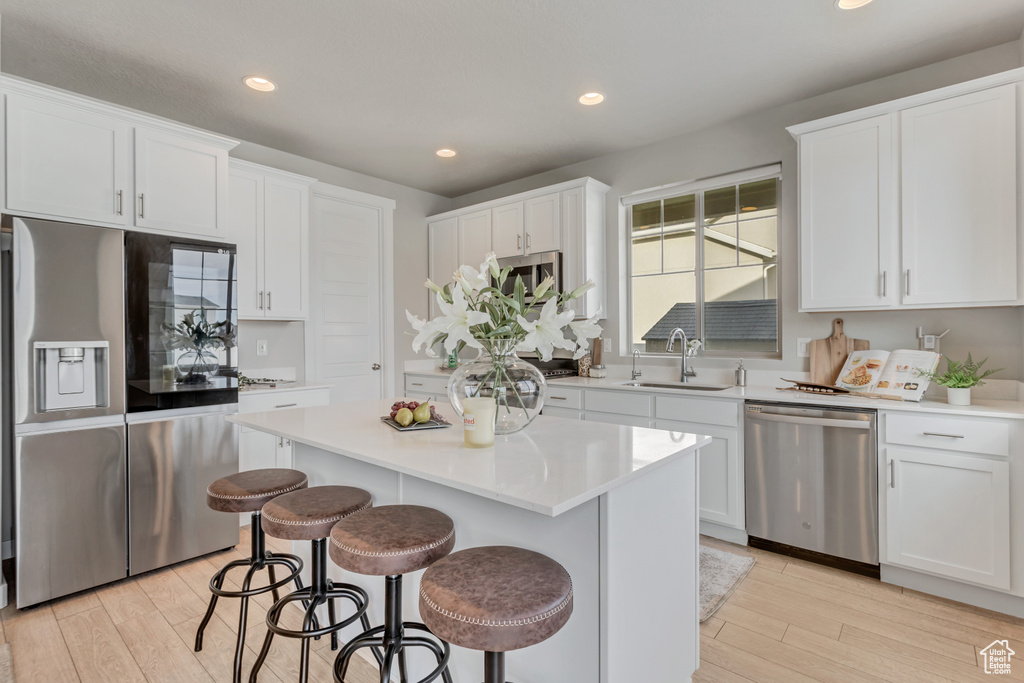 Kitchen with white cabinets, stainless steel appliances, a breakfast bar area, a kitchen island, and light hardwood / wood-style floors