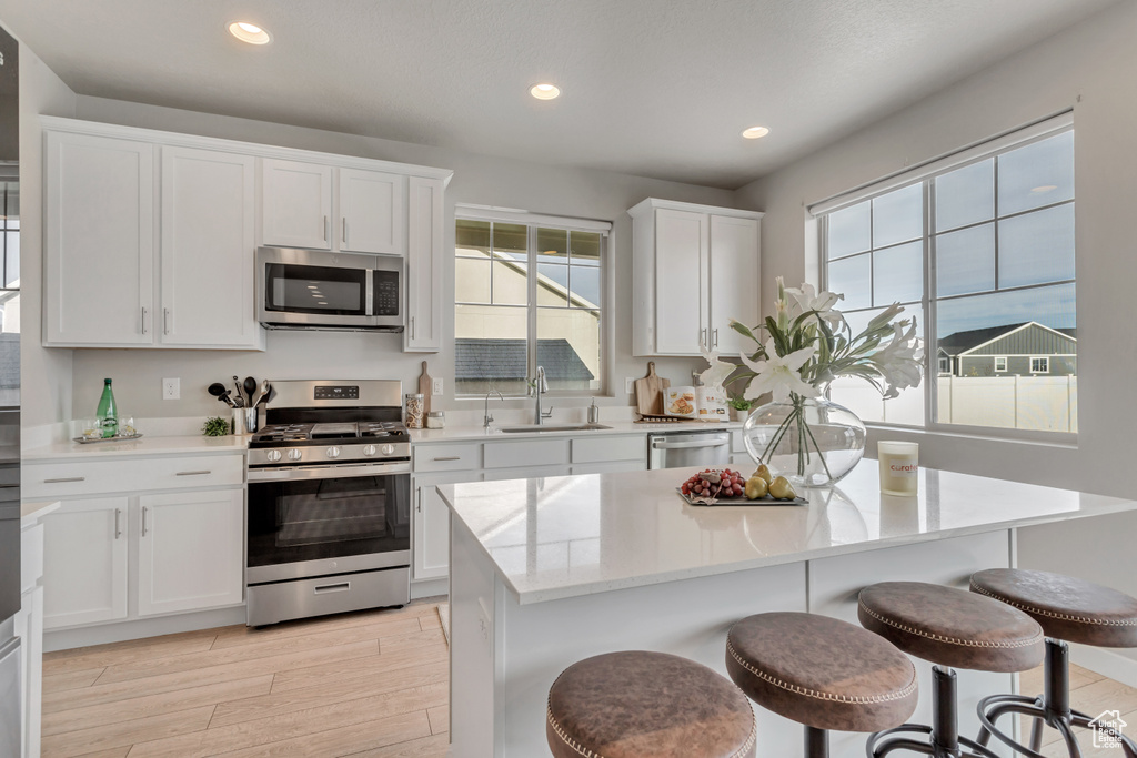 Kitchen featuring white cabinets, stainless steel appliances, light wood-type flooring, and a kitchen bar