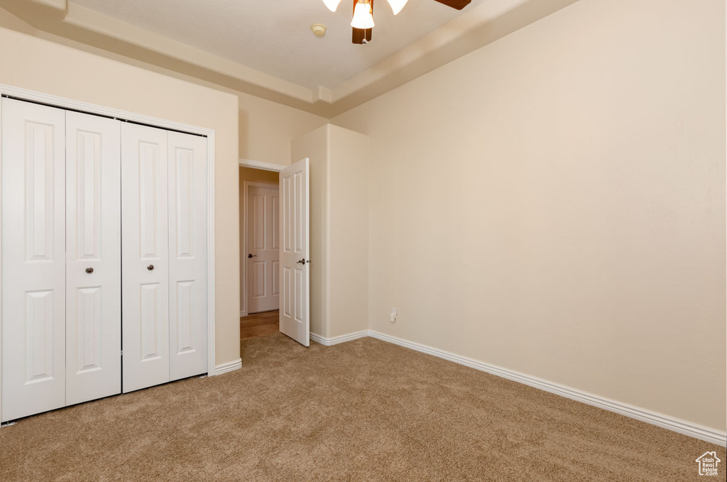 Unfurnished bedroom featuring light colored carpet, a closet, ceiling fan, and a tray ceiling
