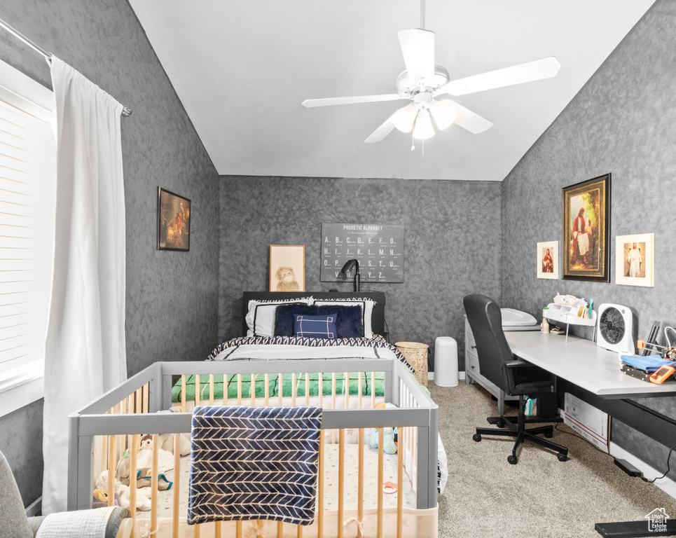 Carpeted bedroom with ceiling fan, a crib, and vaulted ceiling