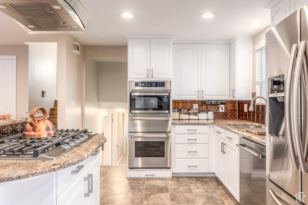 Kitchen with backsplash, stainless steel appliances, white cabinets, and light stone counters