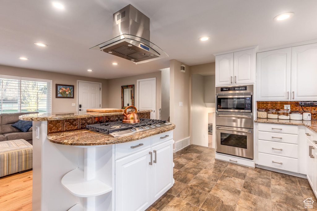 Kitchen with stone countertops, stainless steel appliances, tile floors, white cabinetry, and island exhaust hood