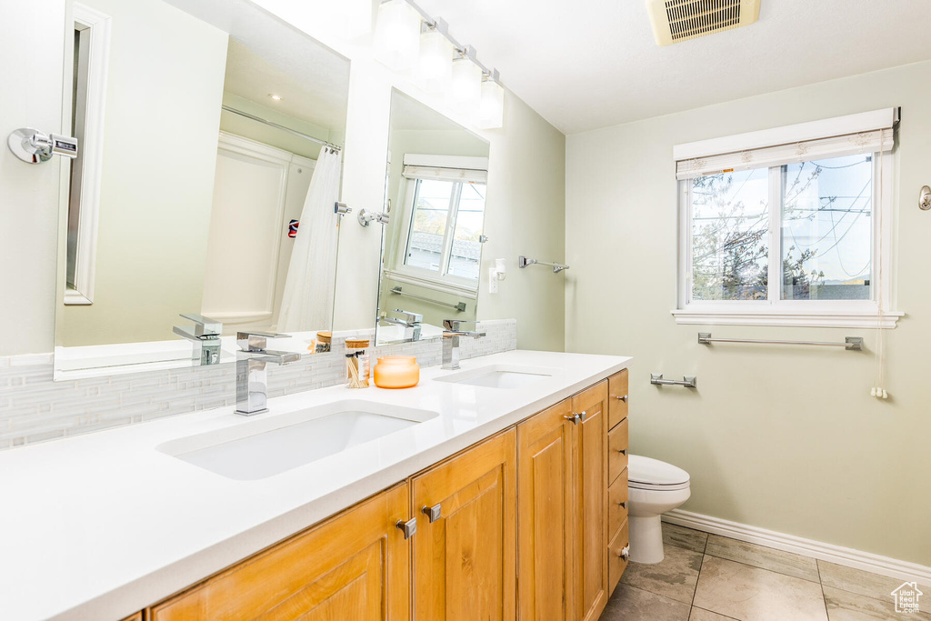 Bathroom featuring oversized vanity, toilet, tile flooring, tasteful backsplash, and double sink