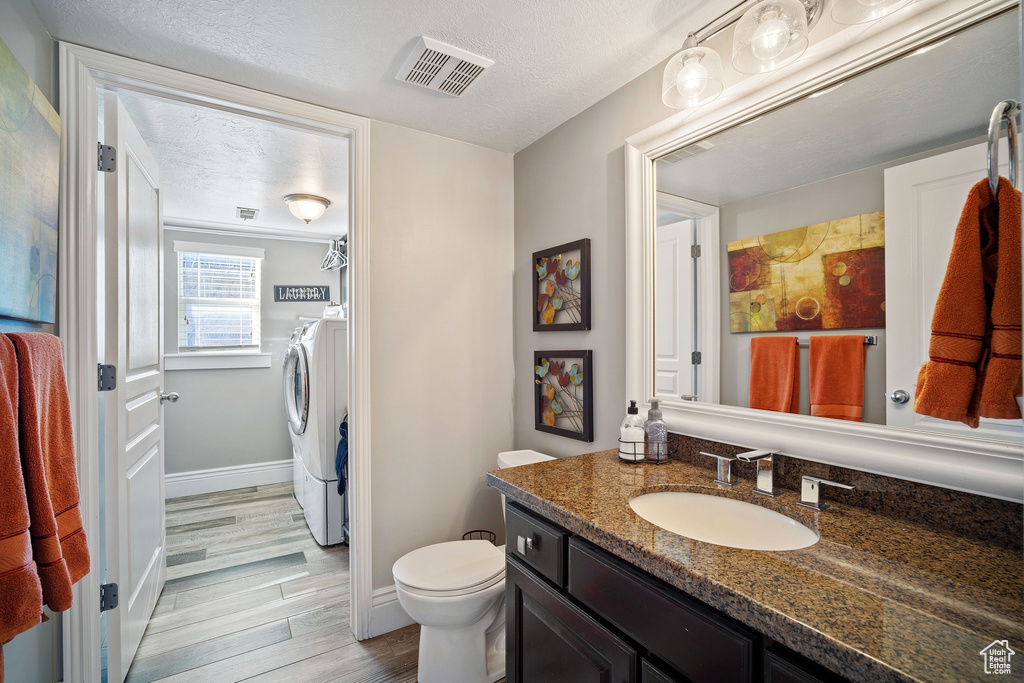 Bathroom featuring vanity with extensive cabinet space, a textured ceiling, washer and clothes dryer, hardwood / wood-style floors, and toilet