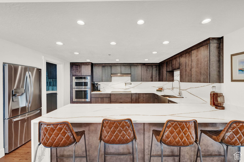 Kitchen with a breakfast bar, light stone countertops, light wood-type flooring, stainless steel appliances, and sink