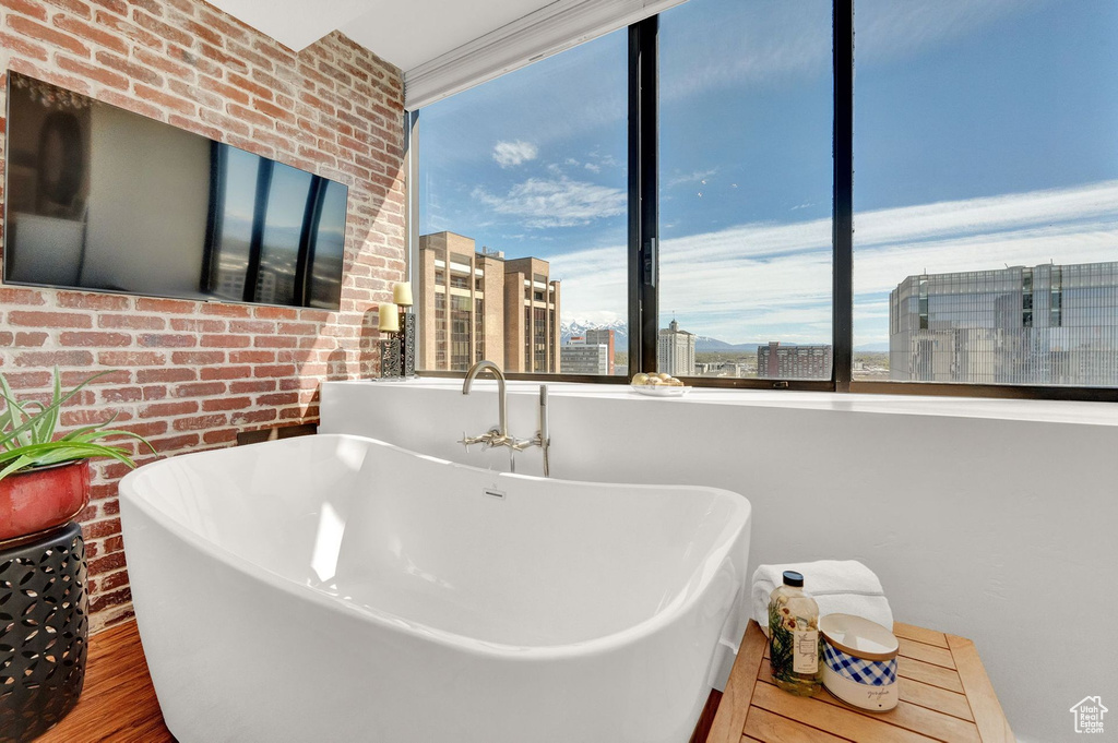 Bathroom featuring wood-type flooring, brick wall, and a bath