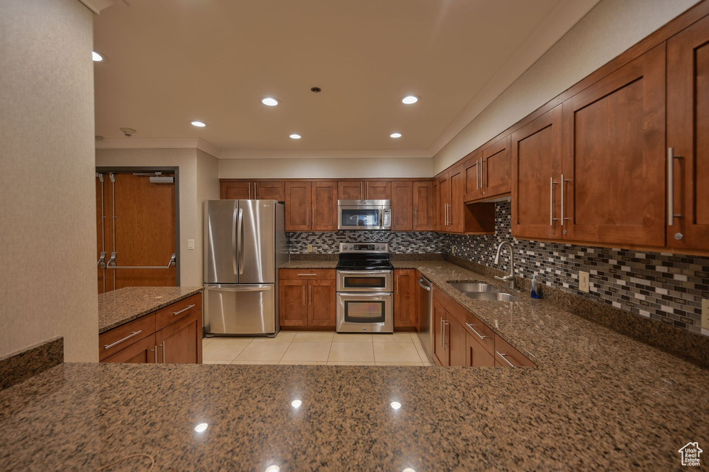 Kitchen featuring appliances with stainless steel finishes, sink, backsplash, light tile flooring, and dark stone countertops