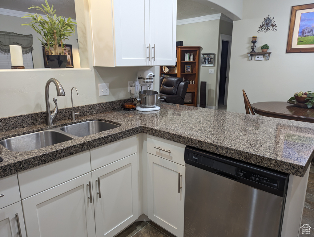 Kitchen with dishwasher, dark stone counters, white cabinets, sink, and ornamental molding