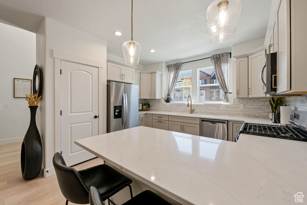 Kitchen featuring tasteful backsplash, appliances with stainless steel finishes, decorative light fixtures, and light hardwood / wood-style flooring