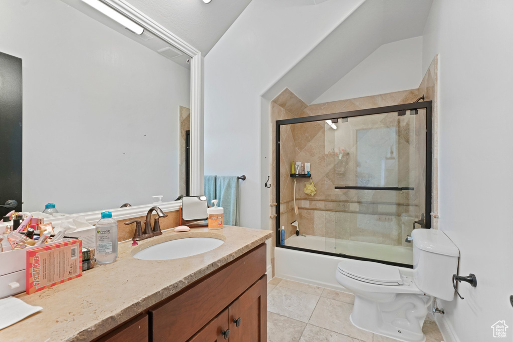 Full bathroom with tile flooring, toilet, vaulted ceiling, vanity, and shower / bath combination with glass door