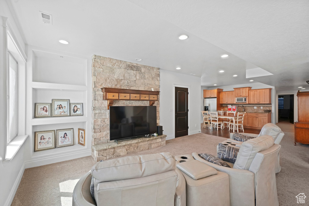 Living room featuring light colored carpet, built in features, and a stone fireplace