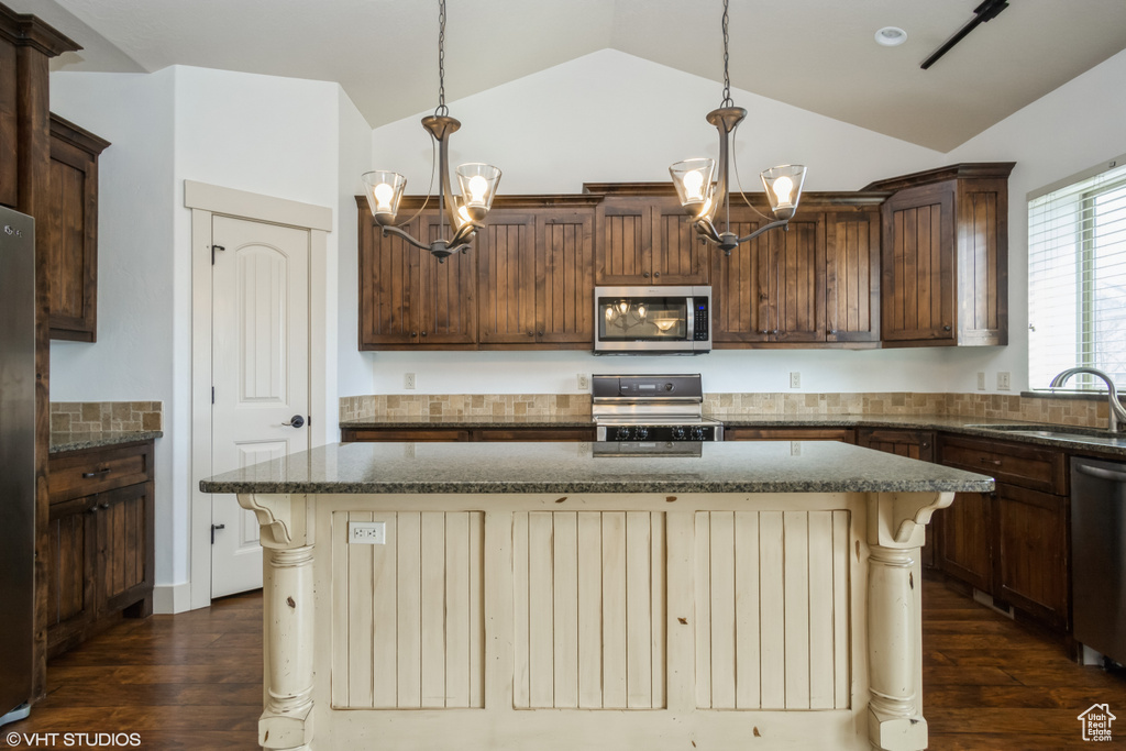 Kitchen featuring a kitchen island, appliances with stainless steel finishes, decorative light fixtures, and vaulted ceiling